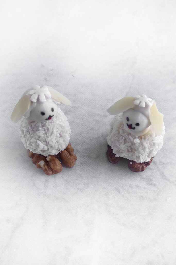 Two Coconut Easter Bunny Candies made from coconut flakes, walnuts, and frosting are placed on a white surface.