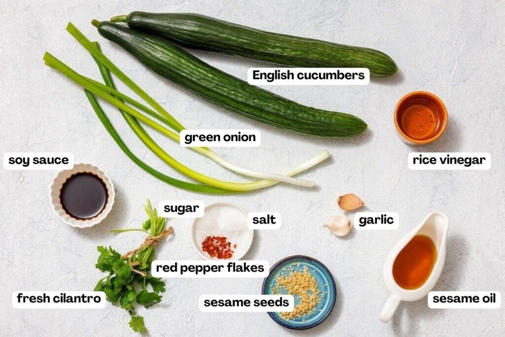 Ingredients on a table include English cucumbers, green onion, soy sauce, rice vinegar, garlic, sesame oil, sesame seeds, red pepper flakes, sugar, salt, and fresh cilantro.