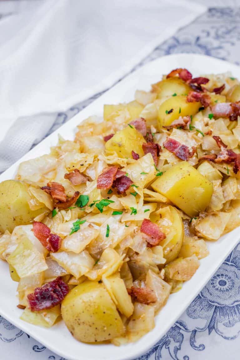 A dish of Cabbage & Potatoes with Bacon garnished with parsley on a white platter.