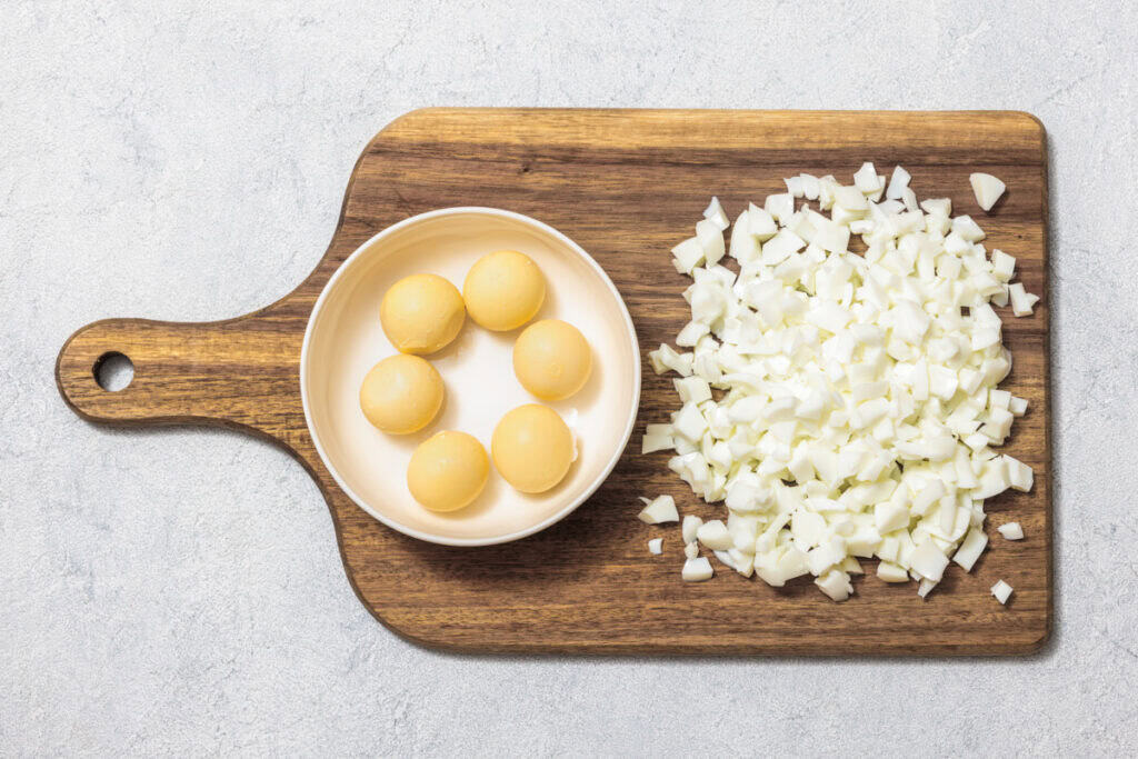 Whole and diced hard-boiled eggs, with yolks in a bowl and whites chopped, on a wooden cutting board.