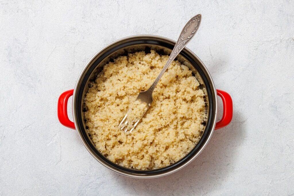 Cooked quinoa in a pot with a red handle, featuring a fork placed inside.