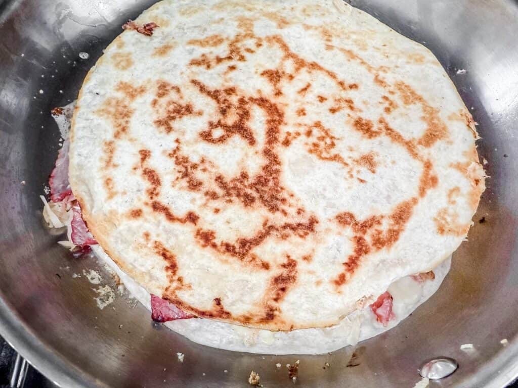 Quesadilla with melted cheese and pieces of meat cooking in a skillet, showing a golden brown and crispy top.
