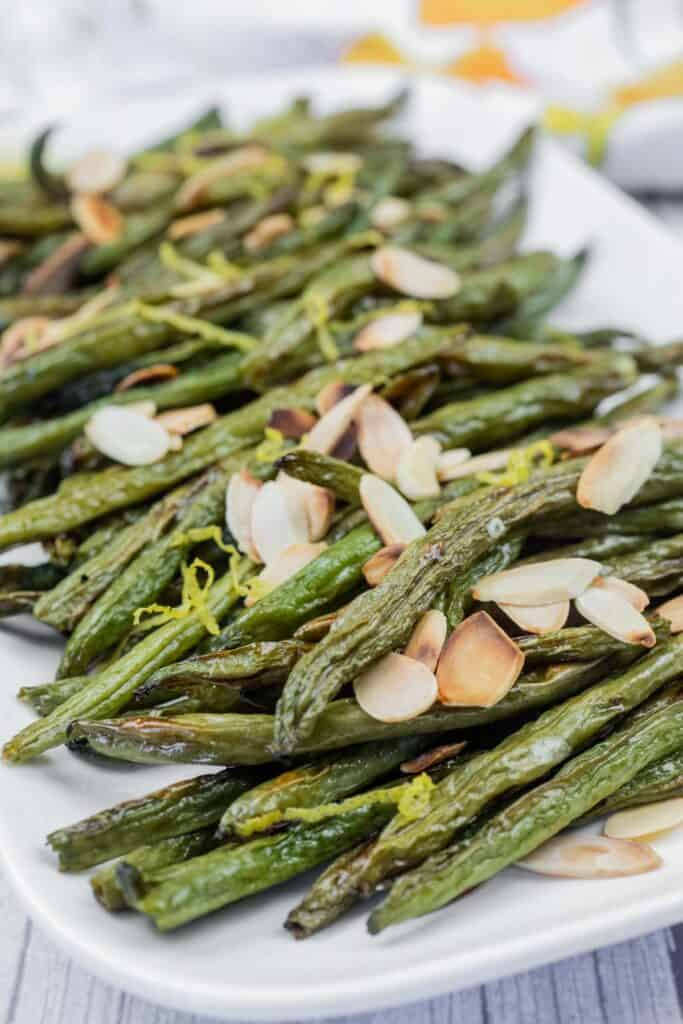 A plate of roasted green beans topped with sliced almonds and lemon zest.