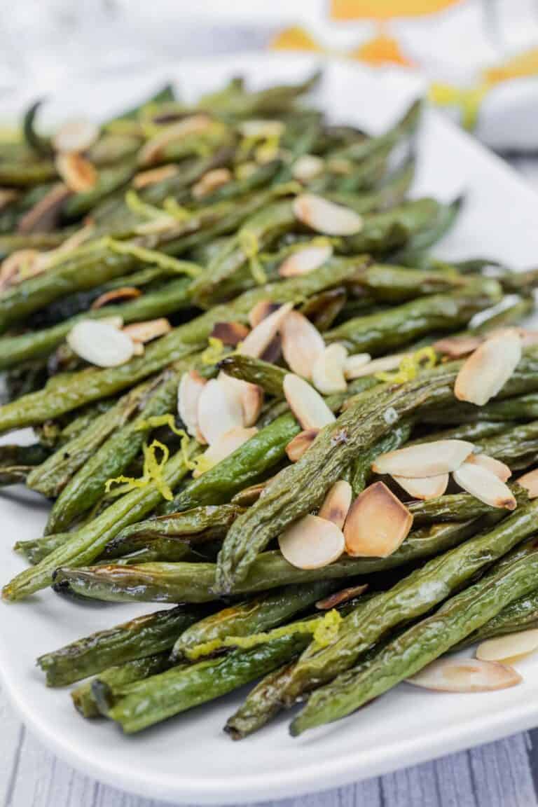 A plate of roasted green beans topped with sliced almonds and lemon zest.
