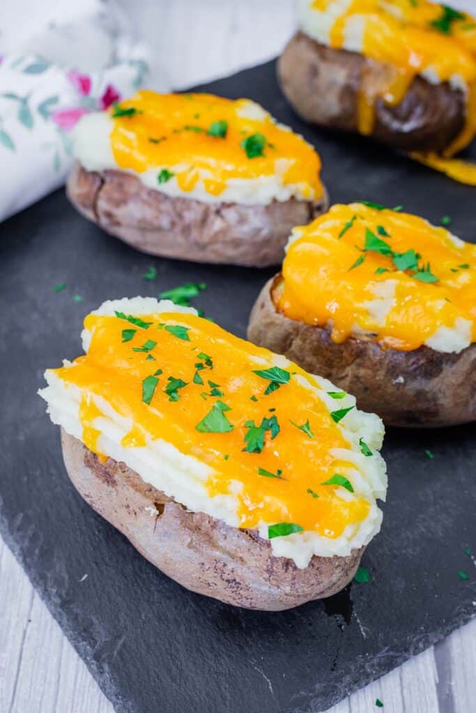 Shepherd’s Pie Baked Potatoes topped with creamy mashed potatoes, melted cheddar cheese, and fresh parsley, served on a black slate board.