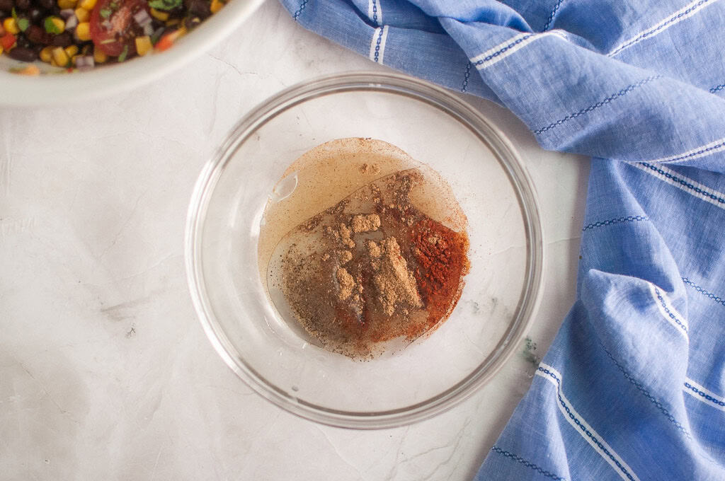 A glass bowl containing various ground spices and liquid, placed on a marble surface next to a blue and white striped cloth.