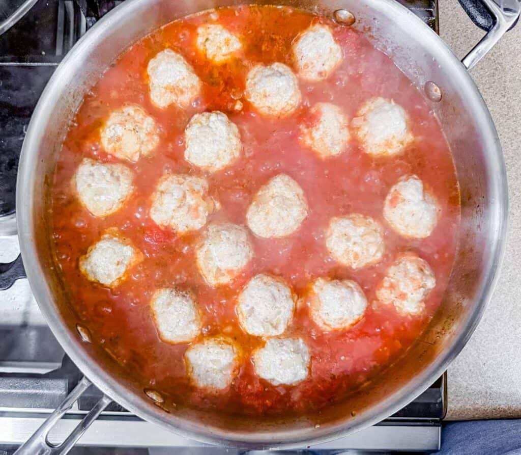 A pan of meatballs cooking in tomato sauce on a stovetop.