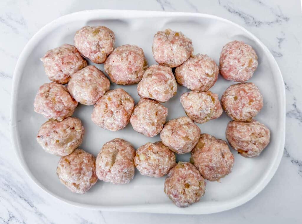 A white tray with evenly spaced raw meatballs on a marble countertop.