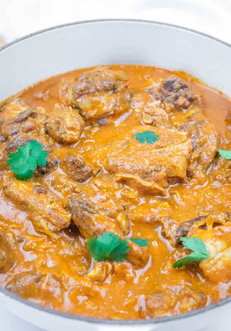 A pot of chicken pieces cooked in a thick, orange-red curry sauce, garnished with fresh cilantro leaves.
