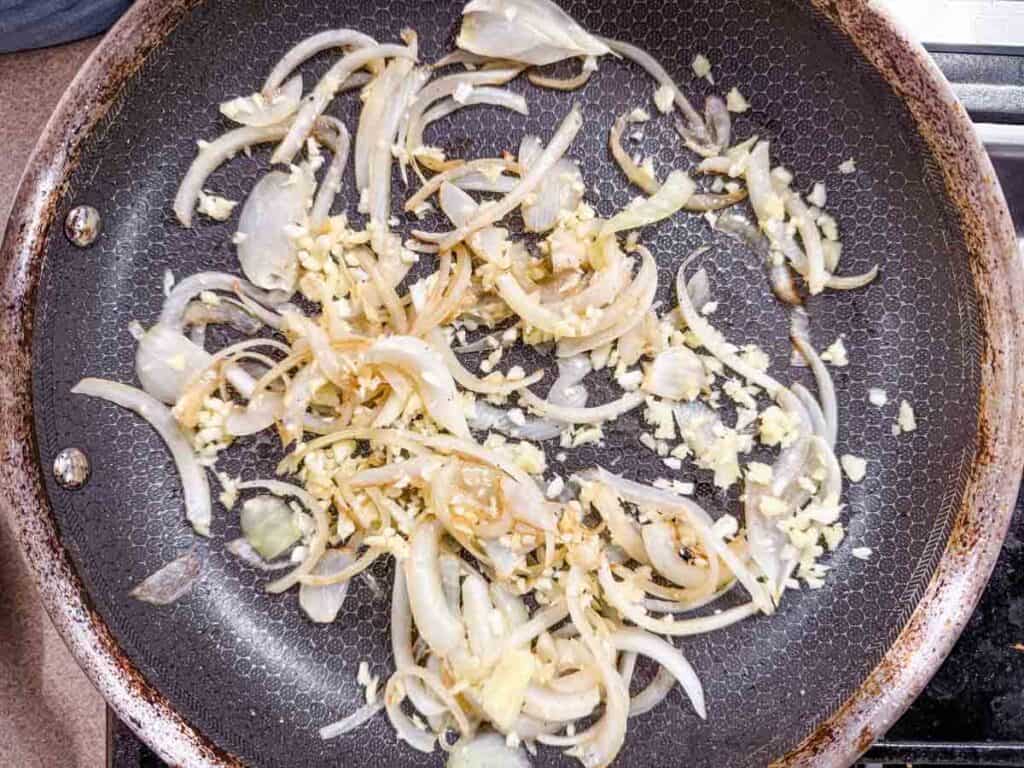 Sliced onions and minced garlic cooking in a nonstick skillet on a stovetop.