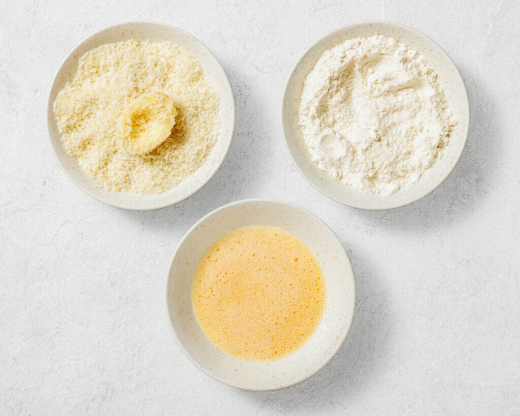 Overhead shot of three bowls with breadcrumbs, flour, and beaten egg, used for breading deviled eggs.
