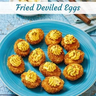 A blue plate with twelve fried deviled eggs, each topped with a swirl of seasoned yolk filling, on a blue-patterned surface.