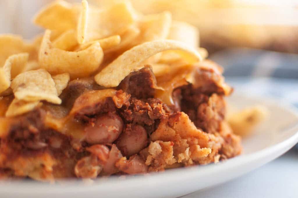 A close up take of Frito Pie in a small white plate on a white table with corn chips on top.