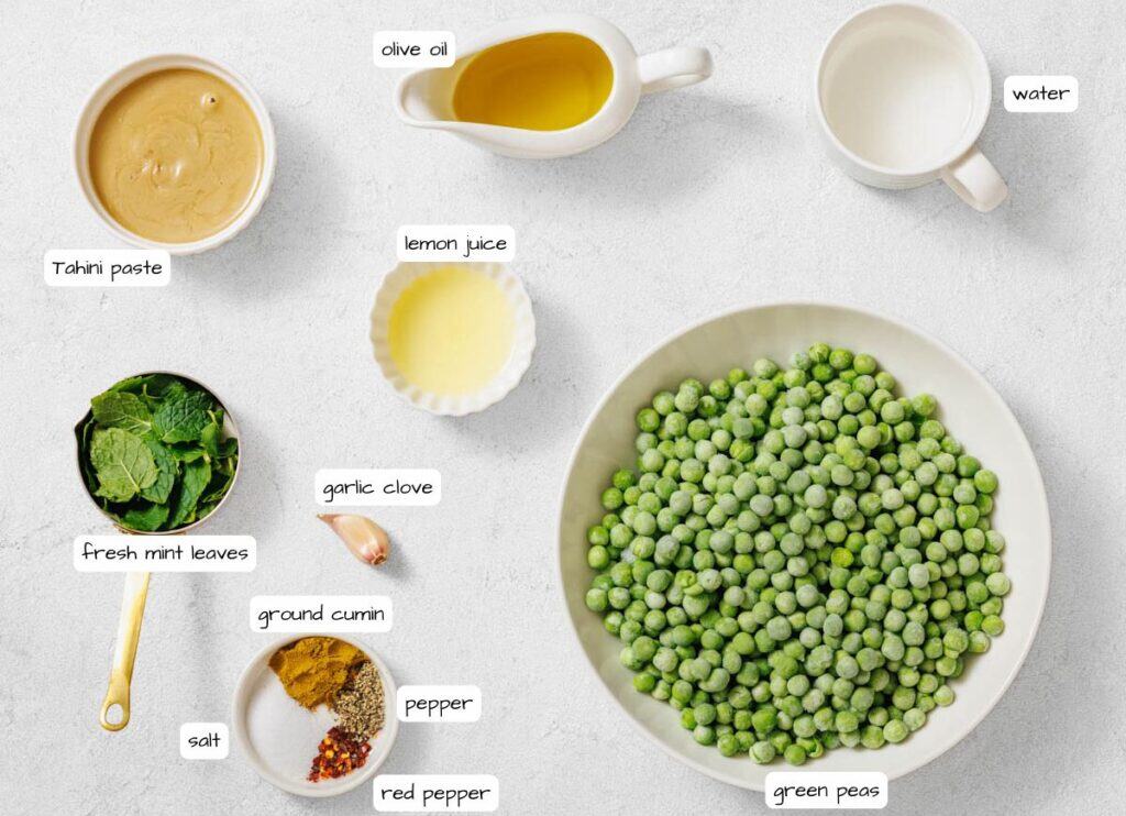 A flat lay of ingredients for a recipe, including green peas, fresh mint leaves, tahini paste, olive oil, lemon juice, garlic, water, ground cumin, salt, pepper, and red pepper.