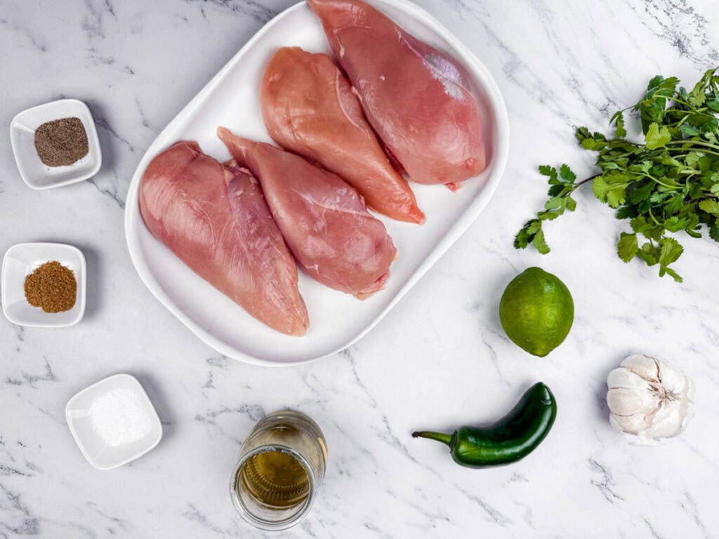 Raw chicken parts, Cilantro, lime, Jalapeno, garlic, oil, salt, cumin powder and black pepper on the surface