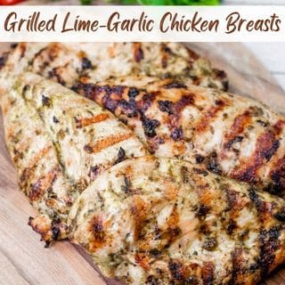 Close-up of grilled chicken on a wooden board with cilantro and tomatoes in the background.