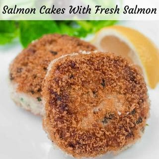 Two Salmon Cakes with a wedge of lemon and mixed greens on a white plate.