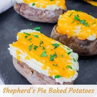 Three baked potatoes topped with mashed potatoes, melted cheddar cheese, and chopped parsley, arranged on a black surface. The text reads "Shepherd’s Pie Baked Potatoes.