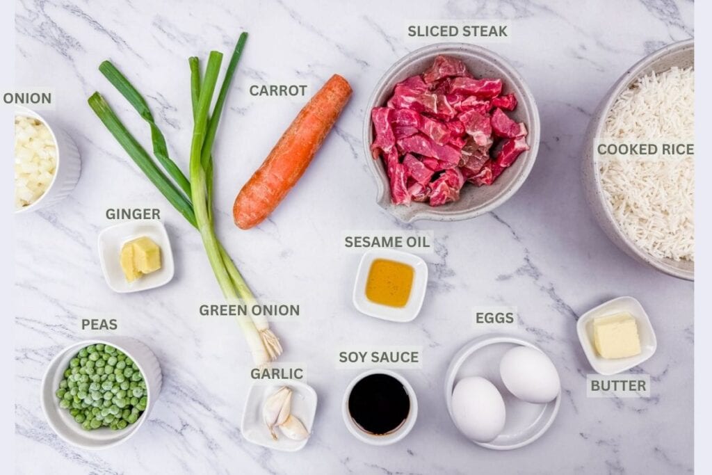 Rice, sliced steak, carrot, oil, eggs, butter, soy sauce, garlic, peeled ginger, sliced onion, green onion, and peas on a marbled white-gray surface with labels