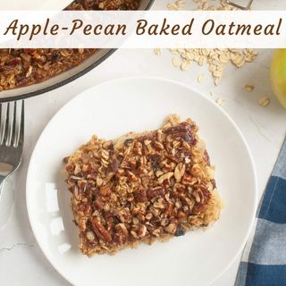 A slice of apple-pecan baked oatmeal sits on a white plate next to a fork, with oats and part of an apple visible in the background.