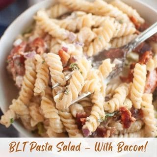 A close-up of BLT Pasta Salad with bacon, lettuce, and tomato in a creamy dressing, being lifted with a fork.