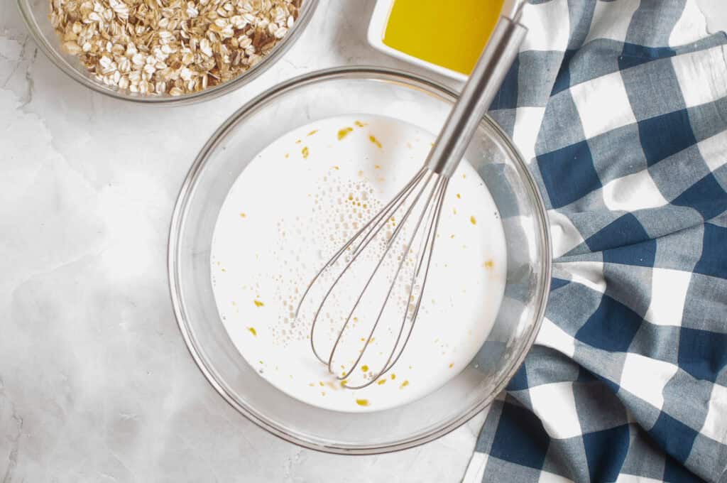 Overhead shot of milk, eggs, and vanilla being mixed in a glass bowl.