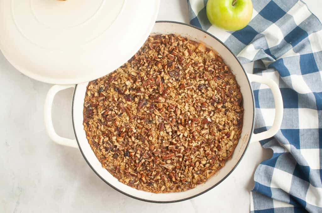 Overhead shot of a golden-brown apple crisp with an oat and pecan topping in a white baking dish.
