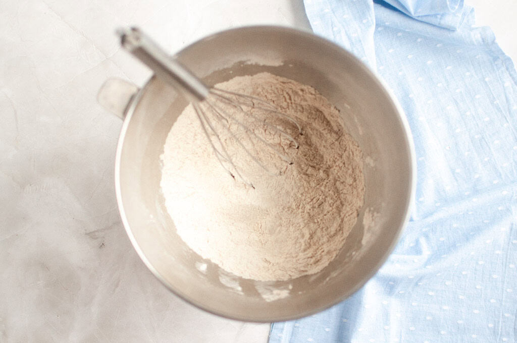 Overhead shot of gluten-free flour and other dry ingredients being whisked in a metal mixing bowl.