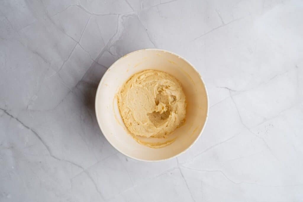 Overhead shot of a light beige mixing bowl containing a smooth, pale yellow cream, possibly almond cream or cookie dough.