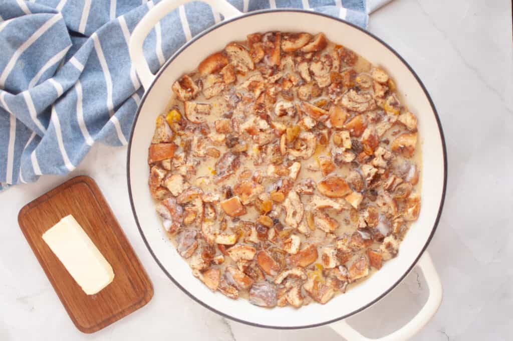 Overhead shot of chopped cinnamon rolls soaking in a light-colored custard mixture in a white pot.