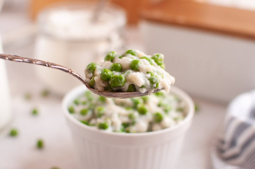 A spoonful of creamy green peas held above a white bowl.