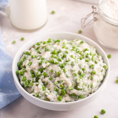 A white bowl filled with a creamy mixture of green peas.