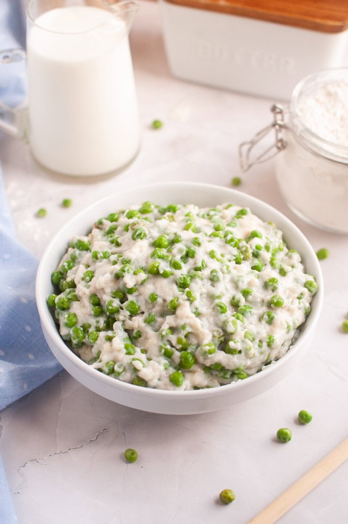 A white bowl filled with a creamy mixture of green peas.