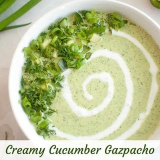 A bowl of light green Creamy Cucumber Gazpacho garnished with fresh herbs and a swirl of cream.