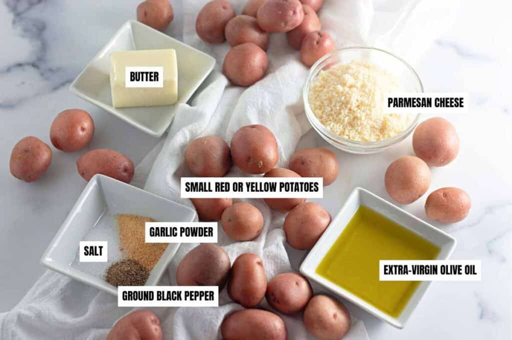 Ingredients for a potato dish are displayed: whole small potatoes, butter, parmesan cheese, olive oil, salt, garlic powder, and ground black pepper.