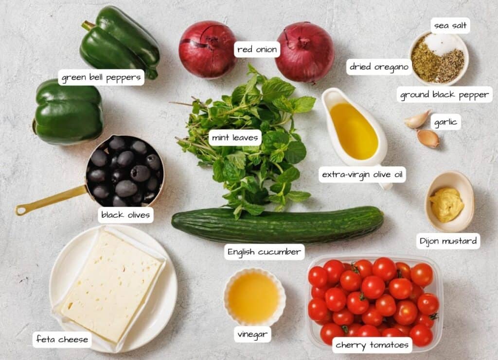 A collection of labeled salad ingredients including vegetables, feta cheese, olives, herbs, spices, vinegar, olive oil, and mustard, arranged on a white surface.