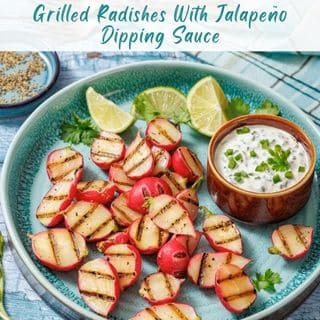 A plate of grilled radish halves with grill marks, served with a creamy jalapeño dipping sauce and lime wedges on a blue plate.