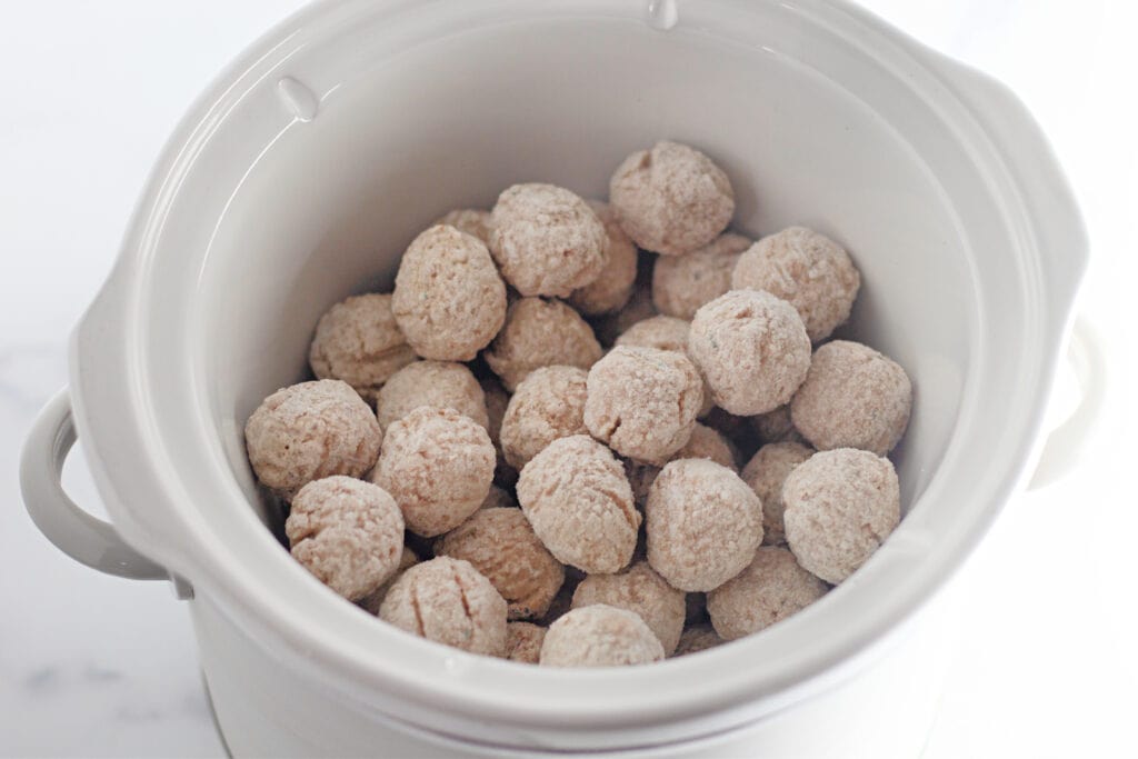 A white ceramic bowl filled with small, round, tan-colored dough balls coated in flour.