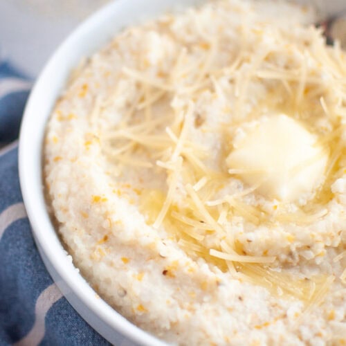 A white bowl filled with creamy grits, topped with shredded cheese and a melting pat of butter.