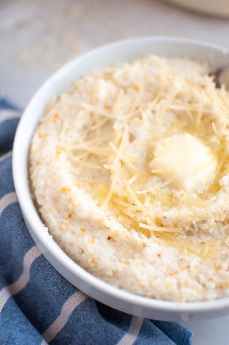 A white bowl filled with creamy grits, topped with shredded cheese and a melting pat of butter.