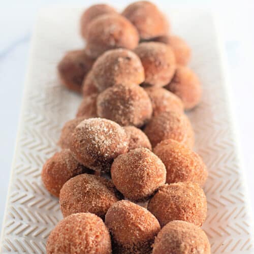 A rectangular plate filled with round, brown sugar-coated doughnut holes arranged in rows.