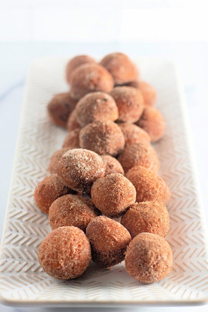 A rectangular plate filled with round, brown sugar-coated doughnut holes arranged in rows.