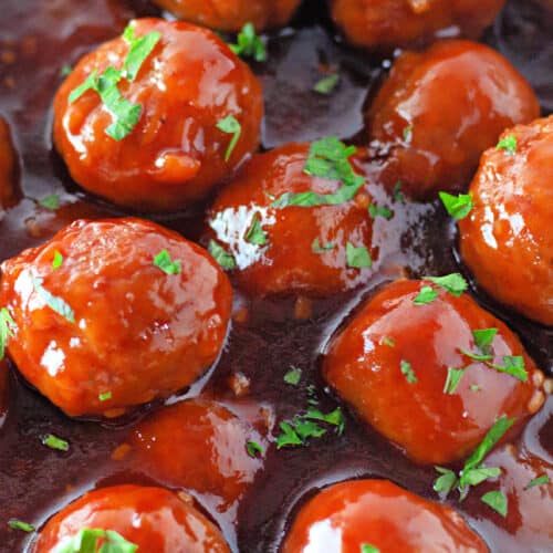 A bowl of meatballs covered in a glossy brown sauce, garnished with chopped fresh herbs.