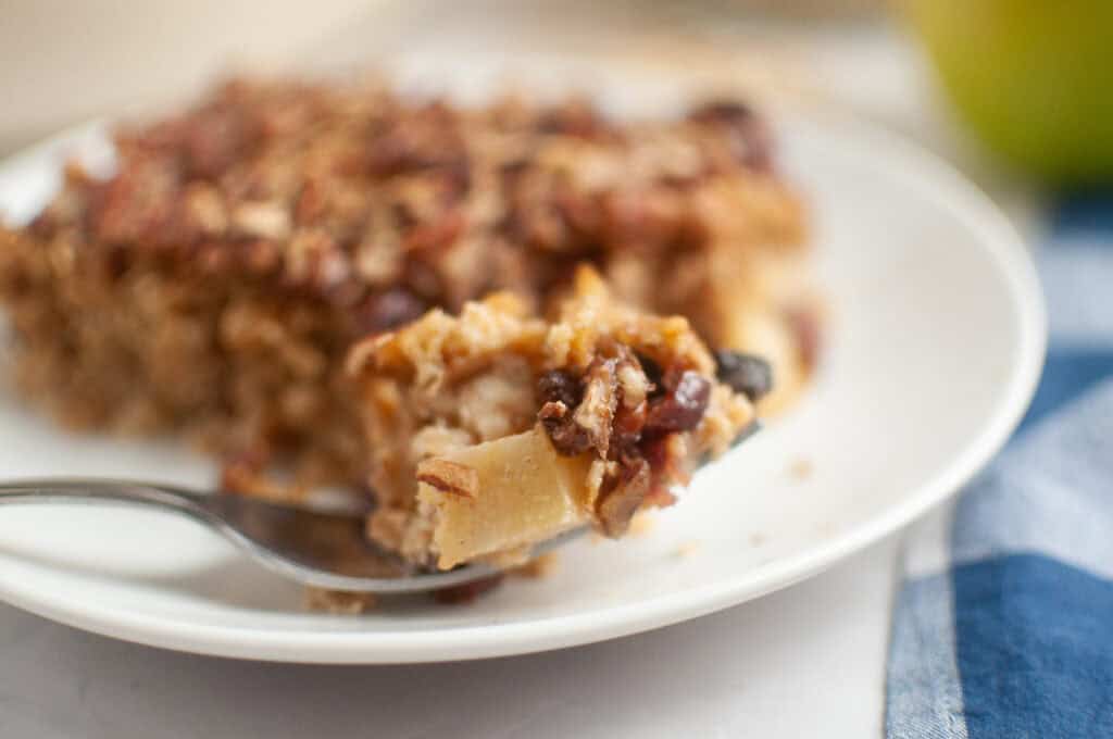 A spoonful of baked oatmeal with visible pieces of apple and pecans, held above a plate.