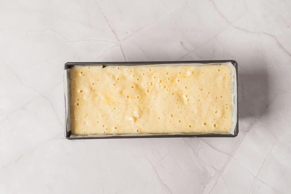Overhead shot of a light yellow lemon olive oil cake batter in a parchment-lined loaf pan.