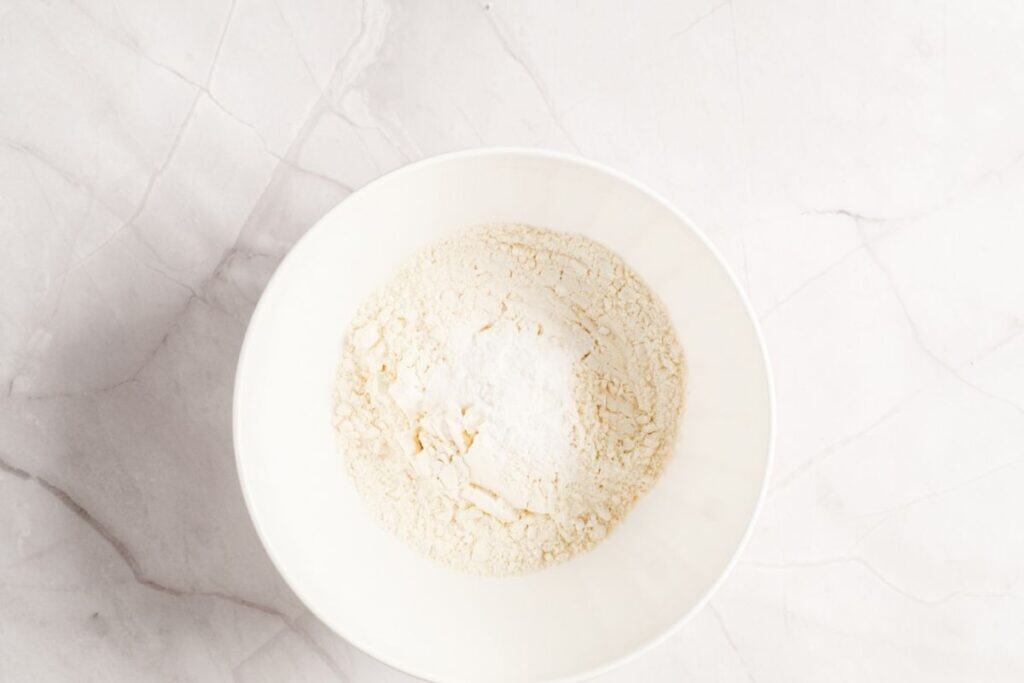 Overhead shot of a white bowl containing flour with a mound of white baking powder in the center.