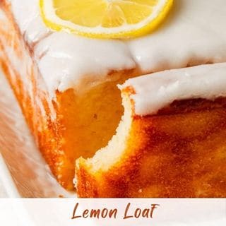 A glazed lemon loaf cake with a slice missing, topped with a lemon slice.