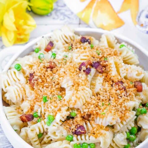 A white bowl filled with Lemony Pasta made with radiatori noodles, green peas, crispy pancetta pieces, and topped with golden toasted breadcrumbs.