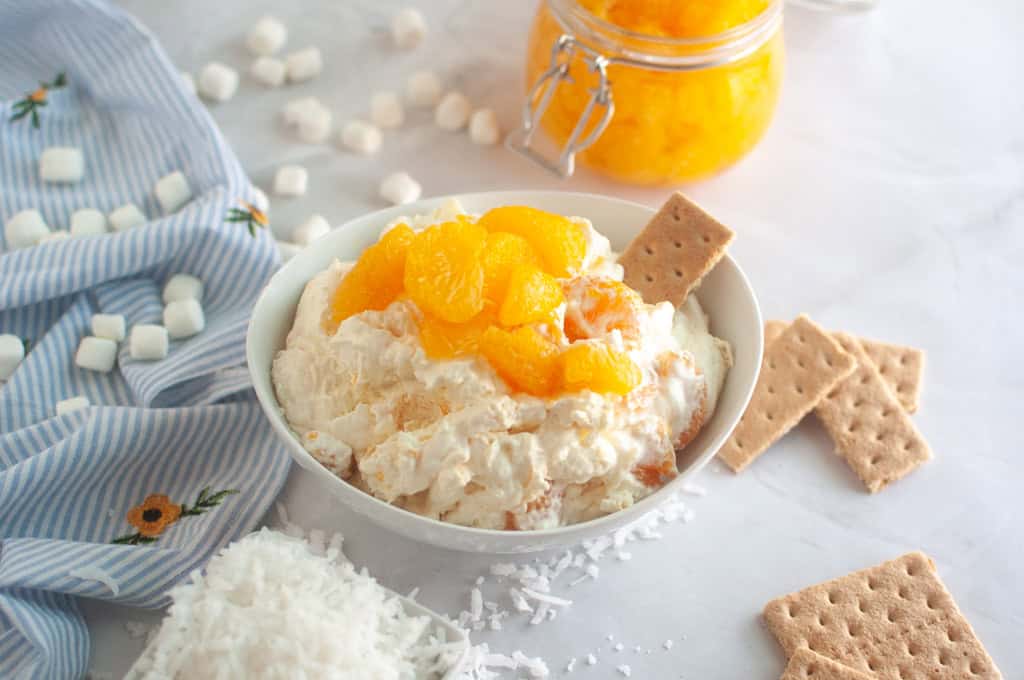 Overhead shot of a white bowl filled with creamy Orange Fluff Salad topped with mandarin oranges and graham crackers.