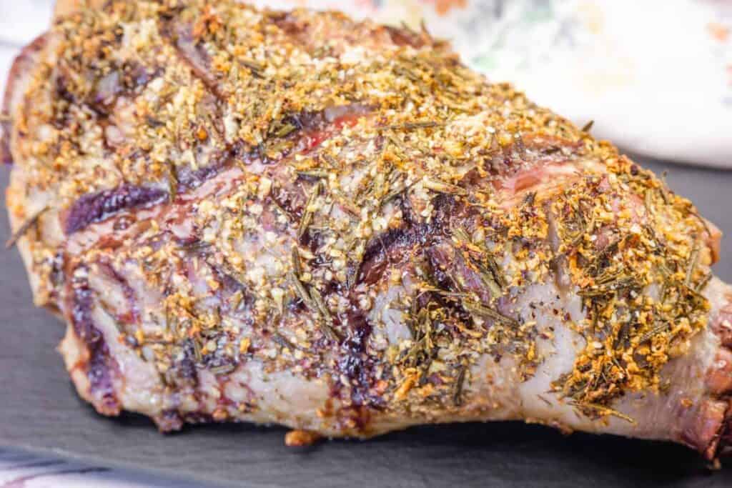 A detailed close-up of a roasted leg of lamb seasoned with herbs and spices.